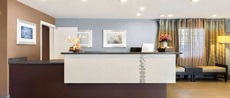 A reception area with a counter, framed artwork, a vase with flowers, a sofa, and a lamp.