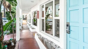 A covered walkway with large windows and a blue door, surrounded by plants and a white exterior. - Sea Blue Hotel (Santa Monica)