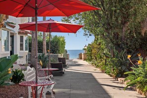 Un sentier bordé de sièges en plein air, de parasols rouges et d’une végétation luxuriante.