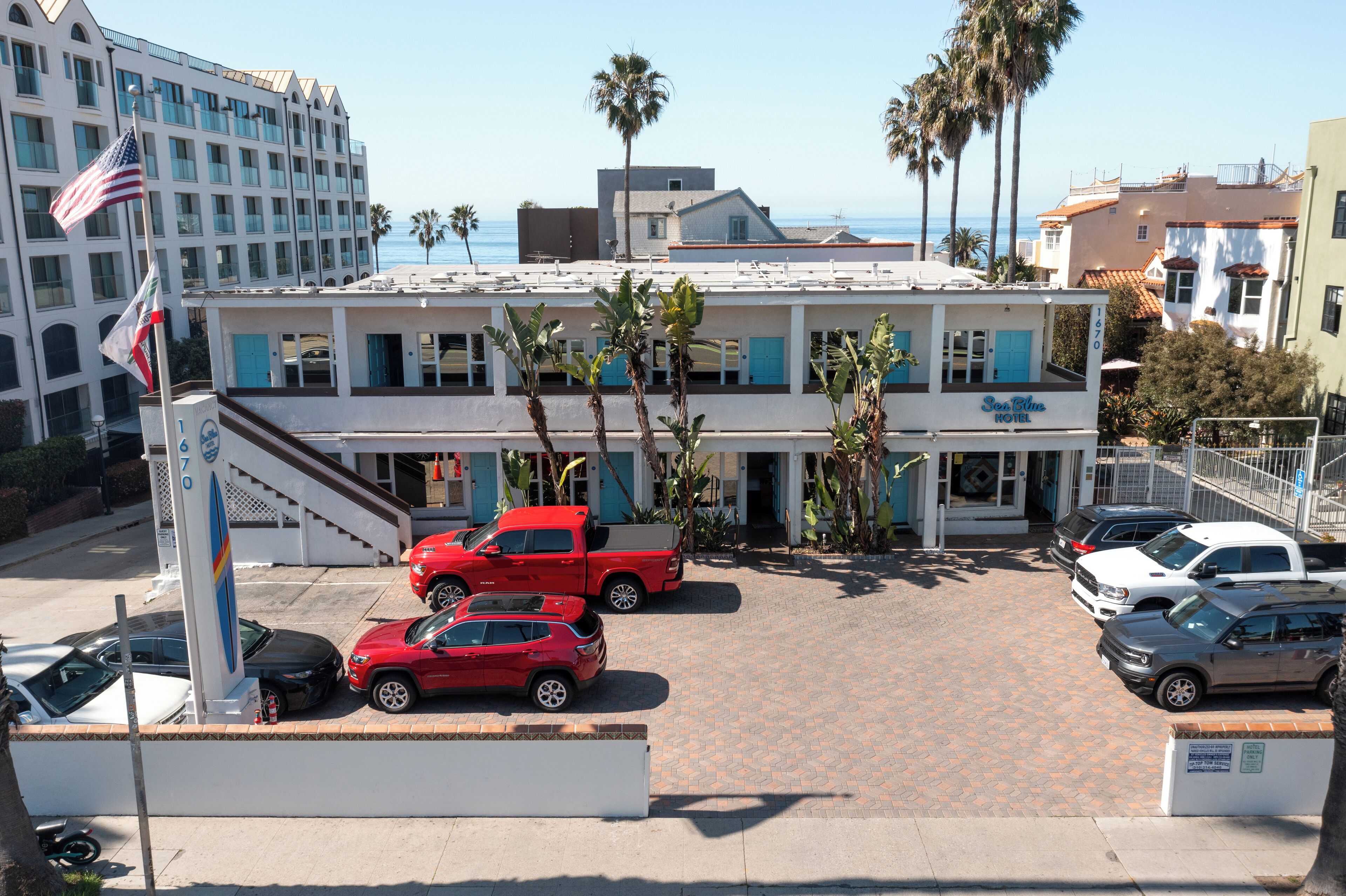 A hotel with a parking lot, palm trees, and a view of the ocean.