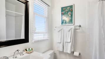 A bathroom with a white sink, a bathtub, a toilet, and a window with blinds. There is a poster on the wall and a towel rack with towels.