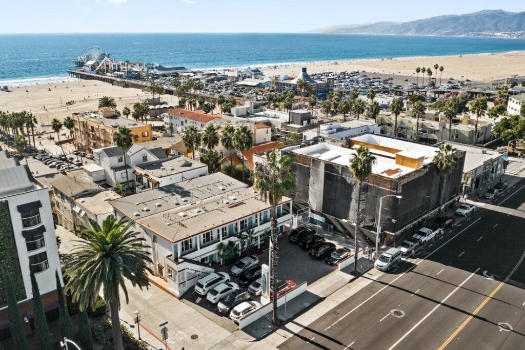 An aerial view of a coastal town with a beach, buildings, and parked cars.