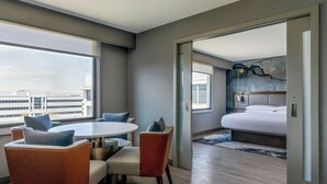 A modern hotel room with a dining area, a large bed, and a city view. - Marriott Denver Airport at Gateway Park (Aurora)
