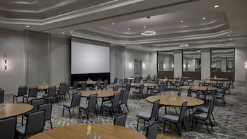 A conference room with multiple round tables and chairs, a large screen, and a carpeted floor.