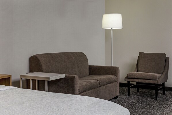 A hotel room with a bed, two armchairs, a small table, and a floor lamp.