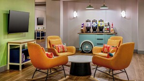 Un espace détente moderne avec des fauteuils à bascule orange, une table basse ronde et un bar équipé de machines à café.