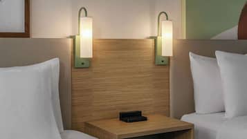 A hotel room with two beds, a wooden headboard, and two wall-mounted nightstands with lamps.