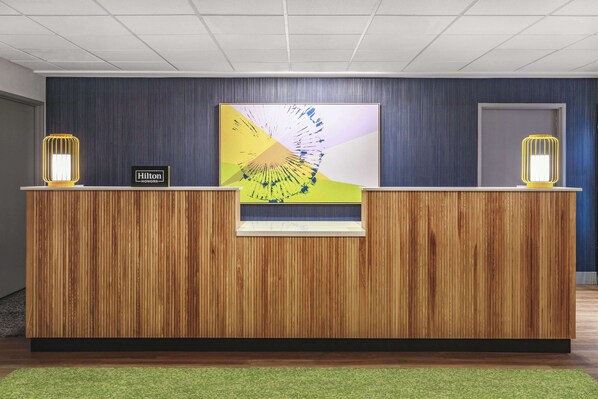 A reception desk with a wooden finish, a large abstract painting above it, and two yellow wall-mounted lamps on either side.