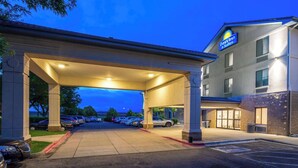Entrada de un hotel con zona de estacionamiento techada, un letrero que dice 'Days Inn & Suites', y un edificio con varias ventanas.