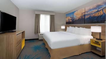 A hotel room with a large bed, a TV, a desk, and a painting of mountains.