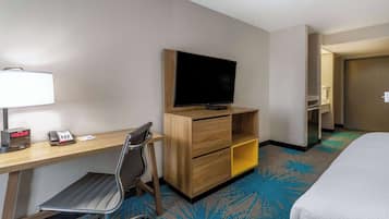 Una camera d'albergo con un letto, una scrivania con televisore, una sedia, una lampada da scrivania e un telefono.