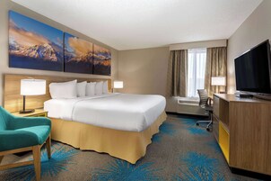 A hotel room with a large bed, two bedside lamps, a desk with a television, a chair, and a window with curtains.