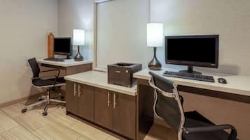 Habitación de hotel con escritorio, dos sillas, computadora, impresora y lámpara.