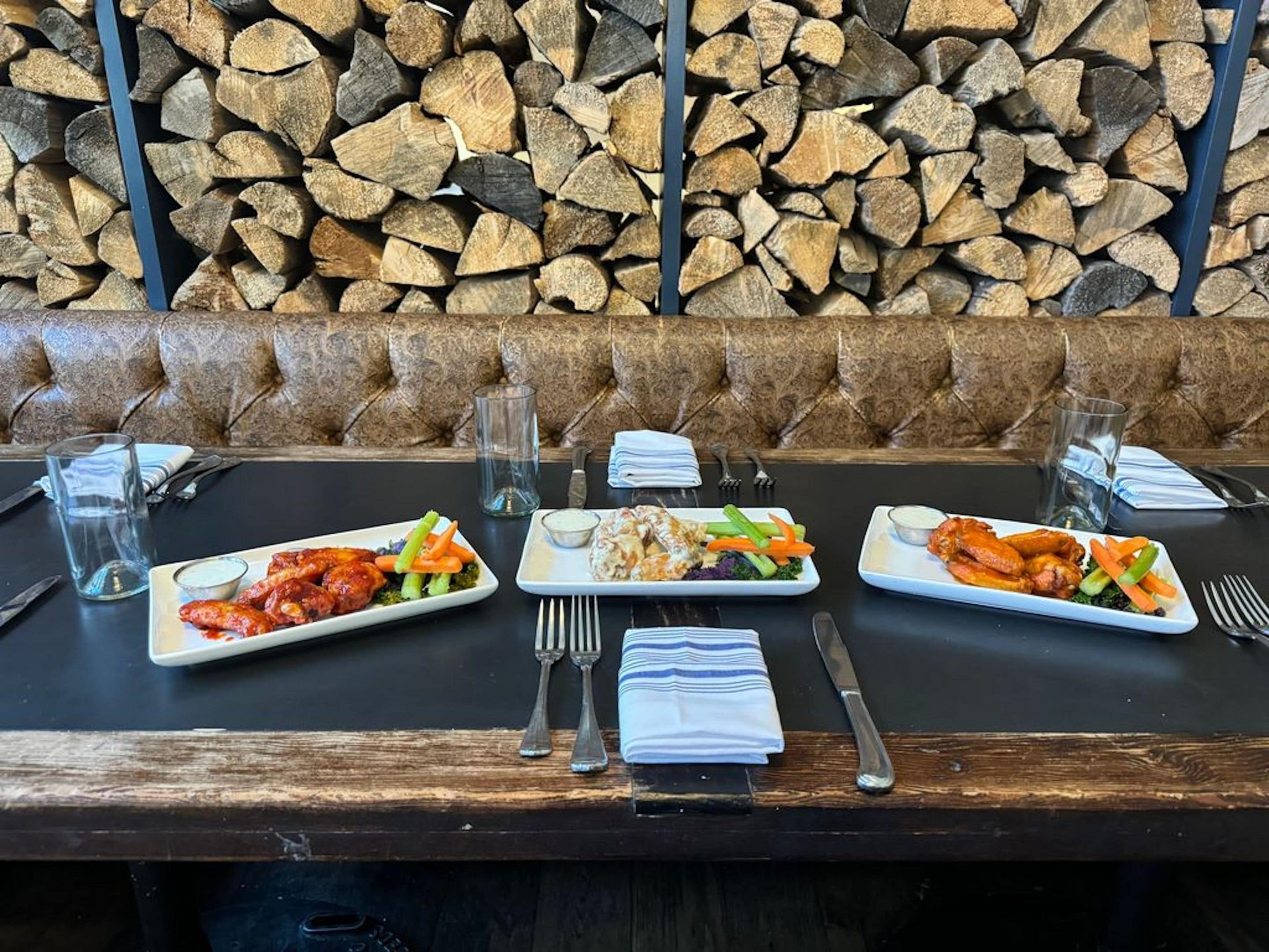 A dining table with three plates of food, glasses, cutlery, and a stack of napkins.