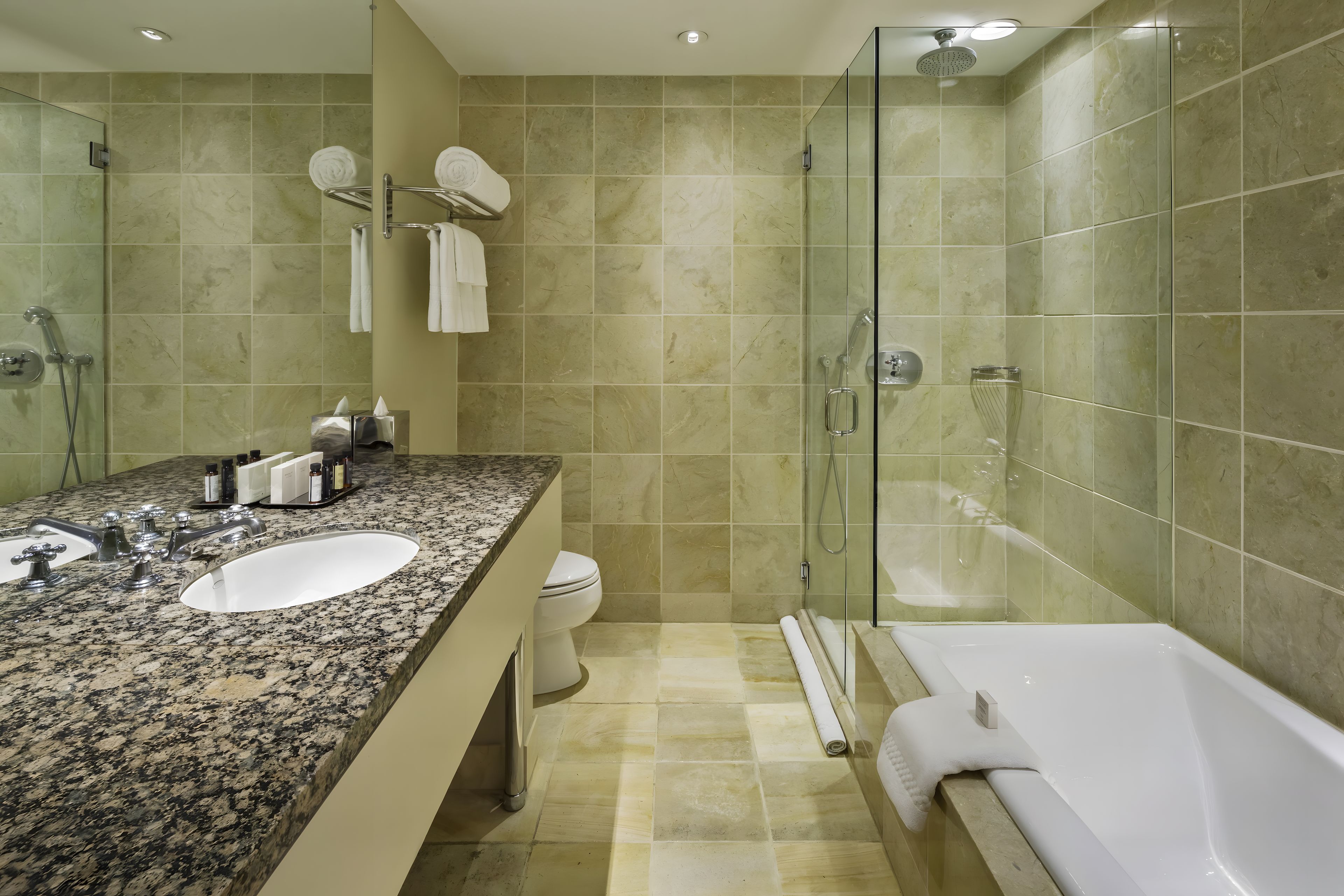 A modern bathroom with a granite countertop, a white sink, a glass-enclosed shower, and a white bathtub.