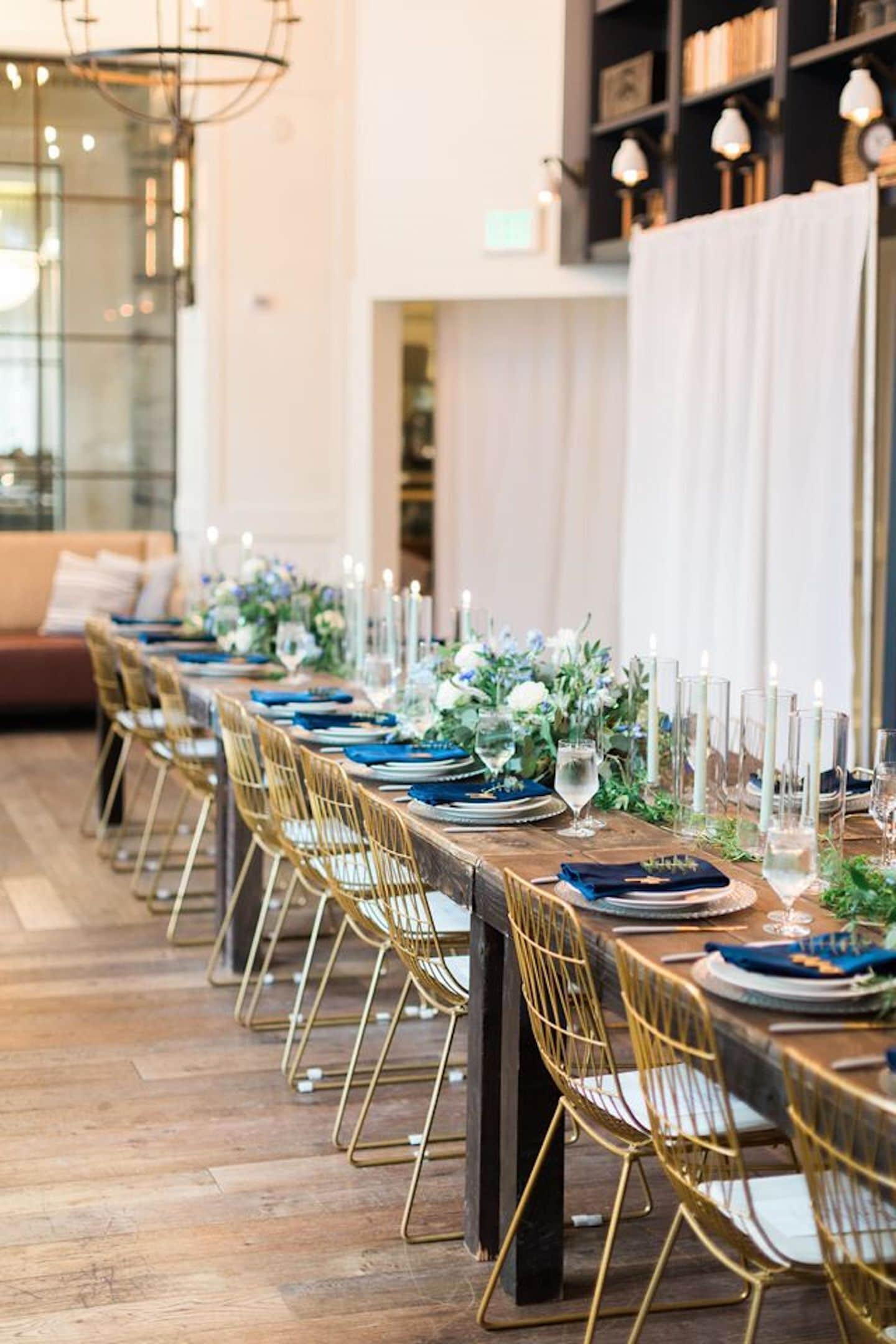 A long dining table with gold chairs, candles, and floral centerpieces.