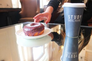 A glass table with a plate of a glazed donut and a large blue cup with "STUDY HOTEL THEATRO" text. - Hotel Teatro (Denver)