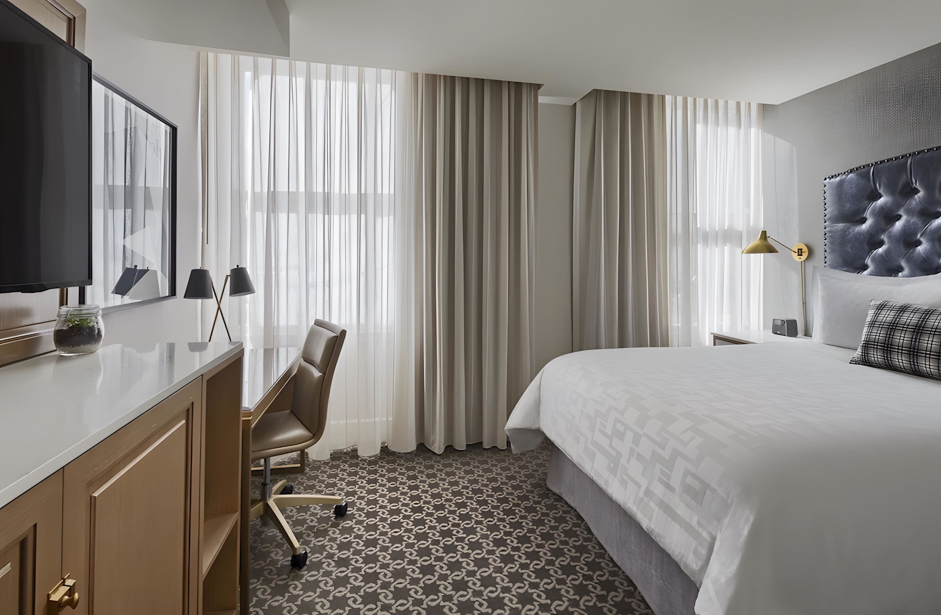 Une chambre d’hôtel avec un lit, un bureau et une chaise, une télévision et des rideaux.