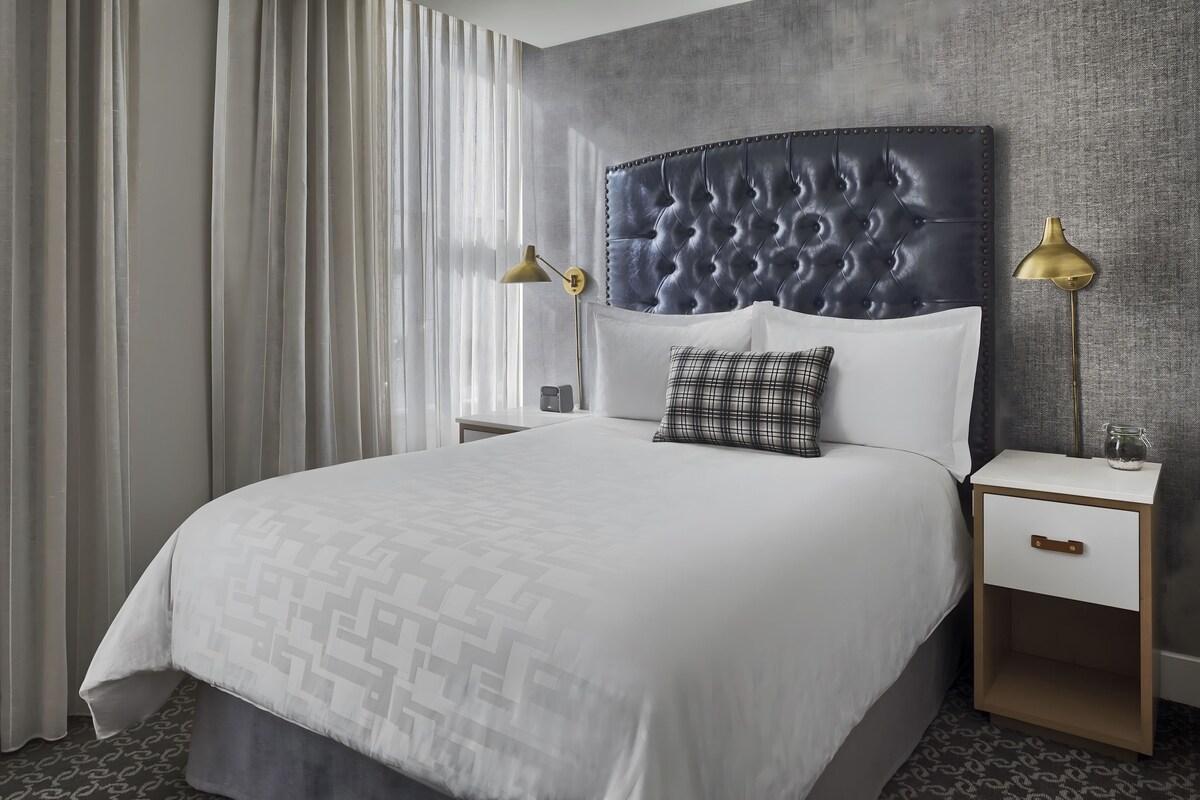 Una habitación de hotel con una cama grande, un cabecero, dos mesitas de noche con lámparas y una alfombra estampada.