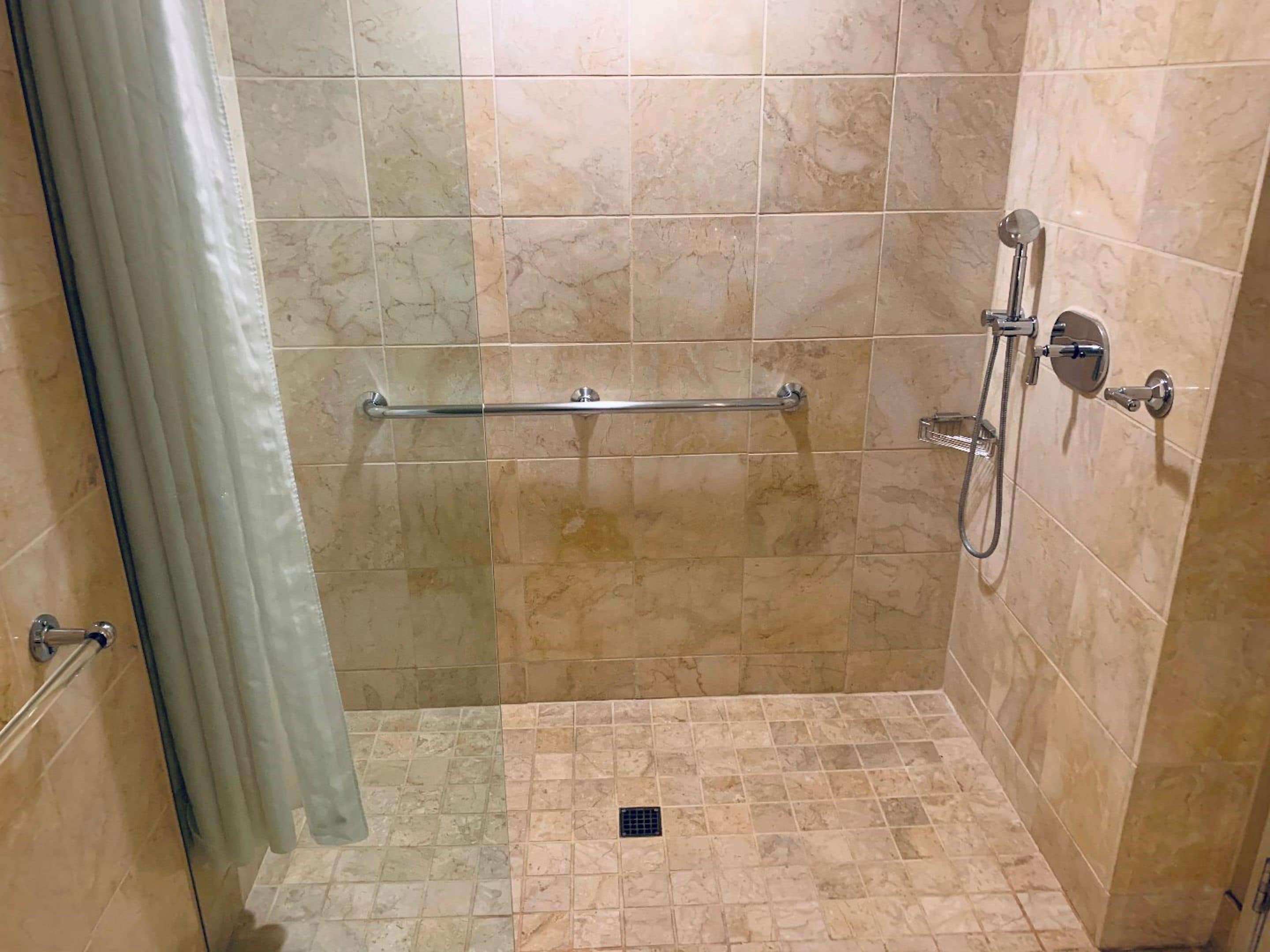 Un espace douche équipé d’une barre d’appui, d’un pommeau de douche à main et d’un drain au sol.