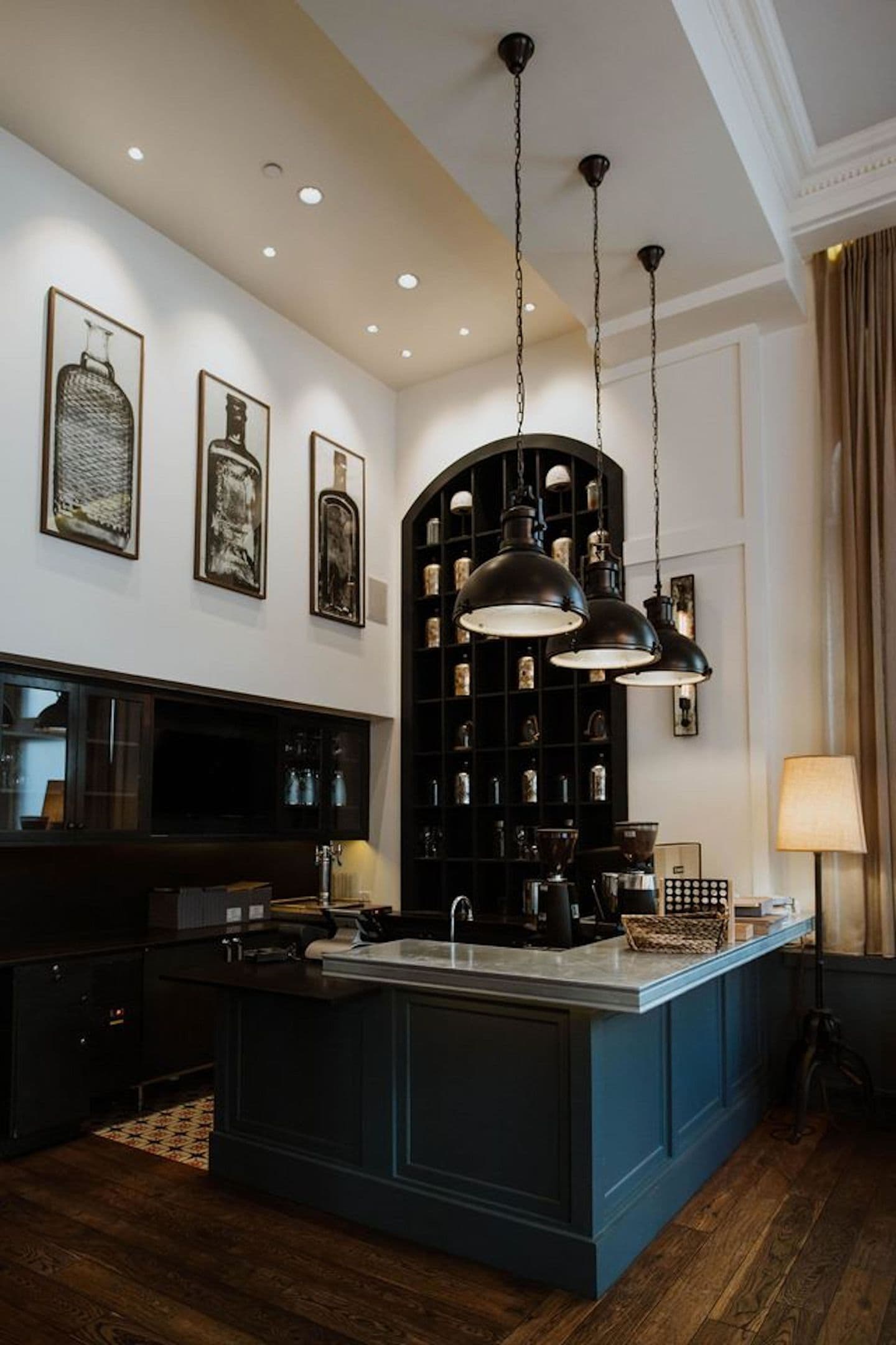 A modern kitchen with a central island, pendant lighting, and a black shelving unit.