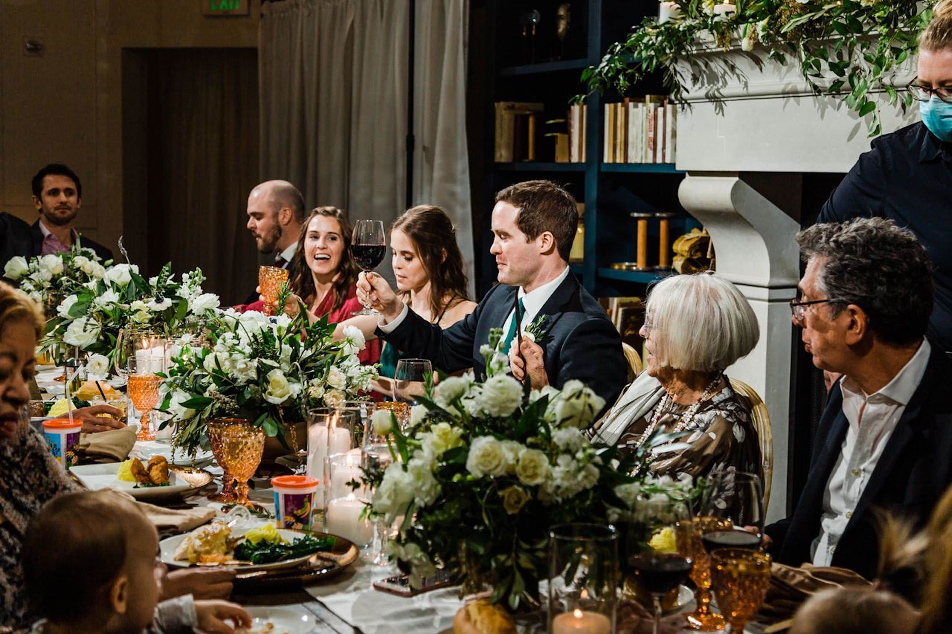 A formal dining setting with guests seated at a table adorned with floral centerpieces and candles.