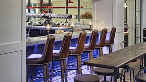 Una zona de bar con taburetes de madera, una barra alargada y estantes con diferentes botellas y vasos.