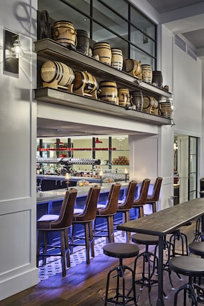 Un espace bar avec des tabourets en bois, un long comptoir et des étagères remplies de différentes bouteilles et de verres.