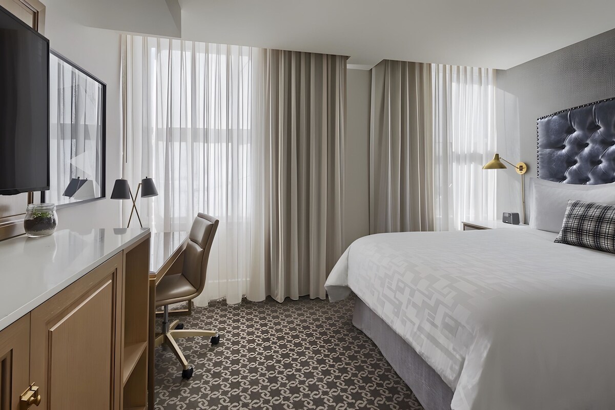 Una habitación de hotel con cama, escritorio, silla, televisor y cortinas.