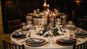 Una mesa redonda de comedor lista para una comida, con varios platos, vasos y velas.