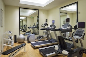 Une salle de sport équipée de tapis de course, de vélos elliptiques, d’un banc et d’un ballon.