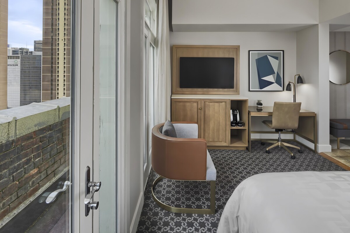 Una habitación de hotel con cama, escritorio, silla, televisión y vistas a la ciudad.