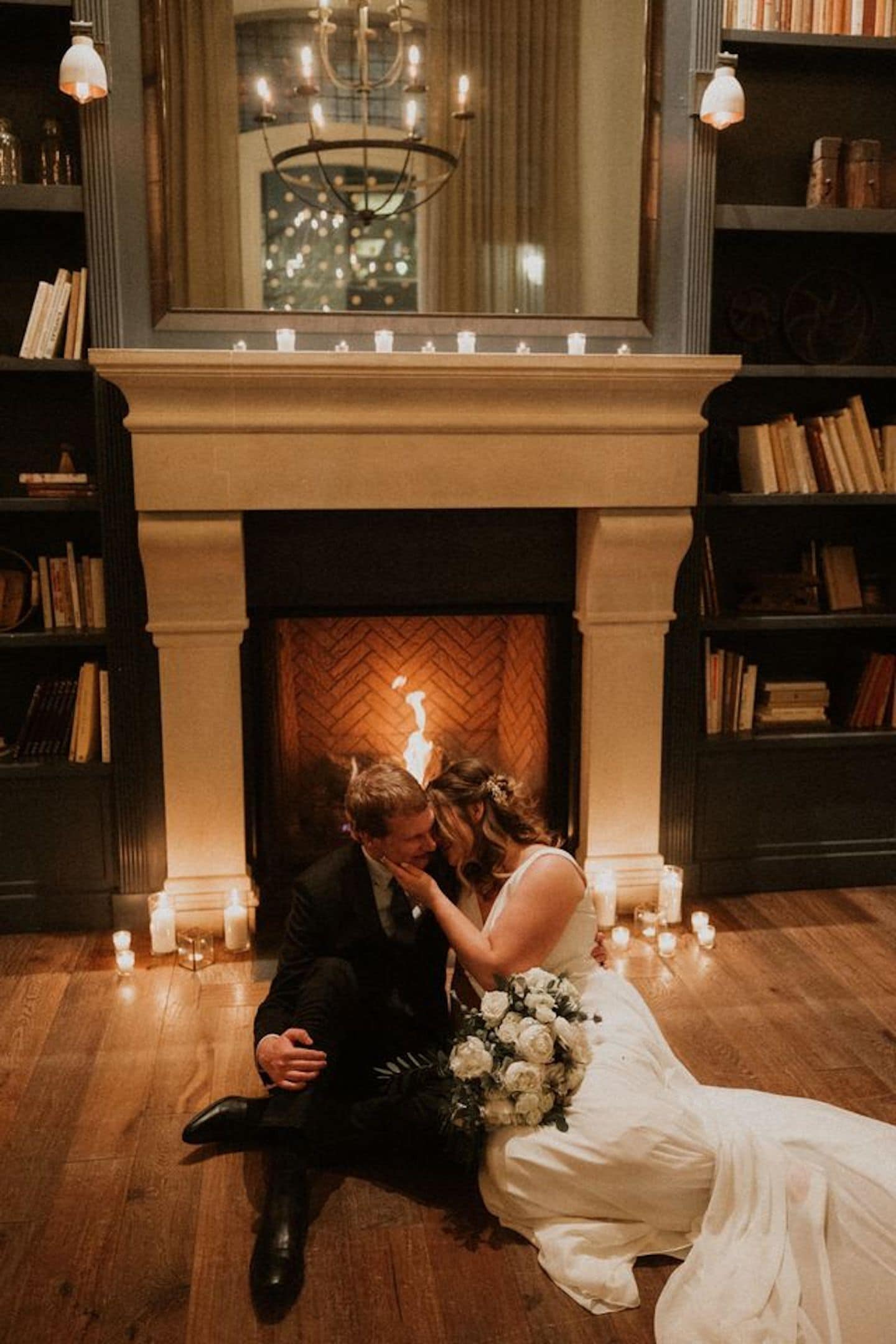 A couple embracing in front of a fireplace with bookshelves on either side.