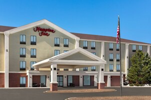 Un hotel Hampton Inn con entrada cubierta, varias ventanas y una bandera estadounidense.
