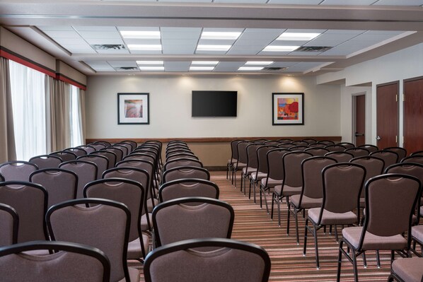 Une salle de conférence avec des rangées de chaises, un téléviseur à écran plat et deux œuvres d’art encadrées accrochées au mur.
