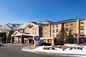 A hotel with a prominent sign, a covered entrance, and a view of mountains in the background.