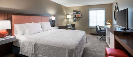 A hotel room with a large bed, a desk with a computer, a TV, and a window with a view.