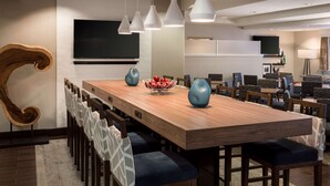 A modern dining area with a long wooden table, blue chairs, and pendant lights. - Hampton Inn-Denver West/Golden (Golden)
