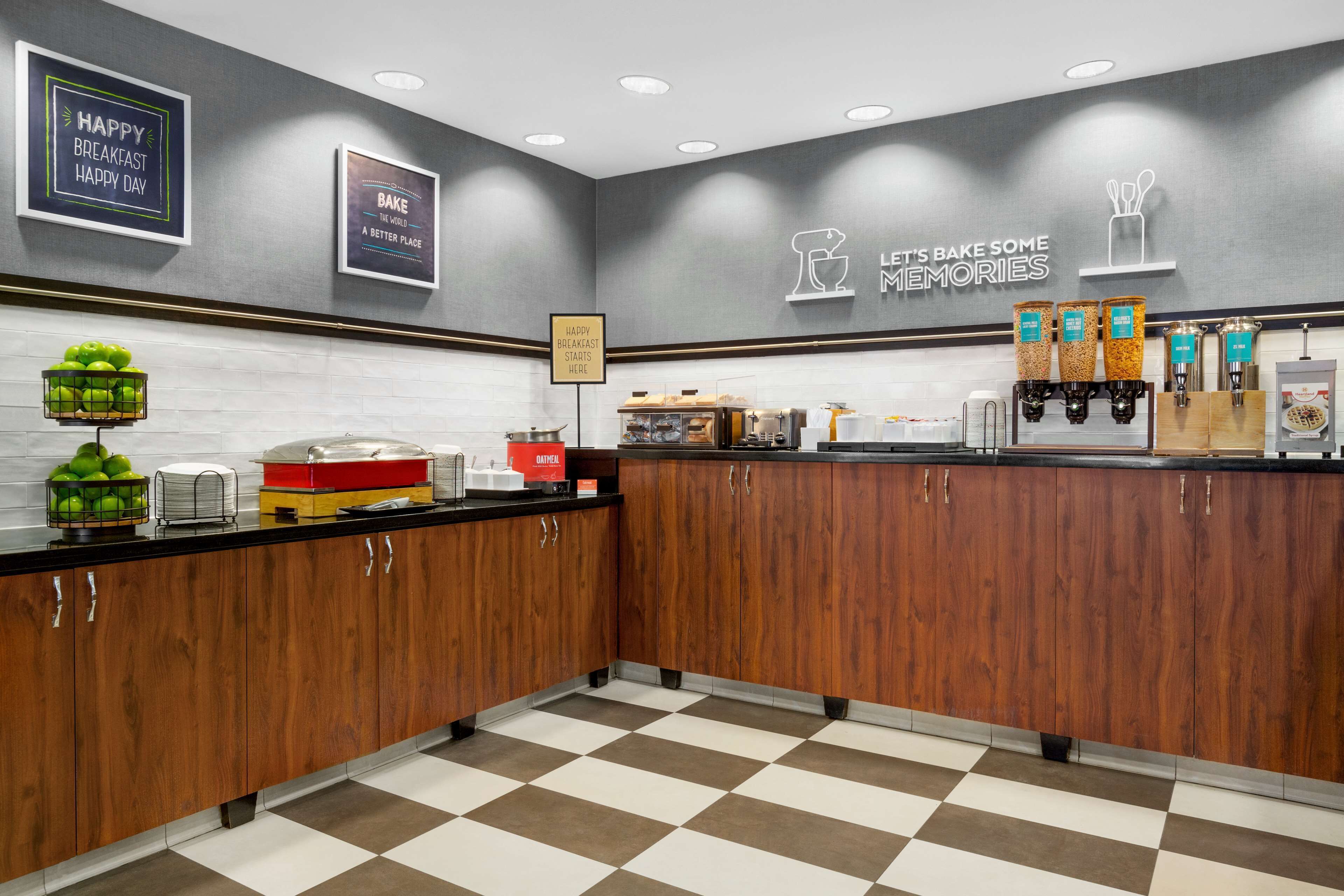 A modern kitchen with wooden cabinets, a checkered floor, and various breakfast items on the counter.