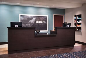 A reception desk with a large 'explore.' poster, a laptop, and a cash register. - Hampton Inn-Denver West/Golden (Golden)