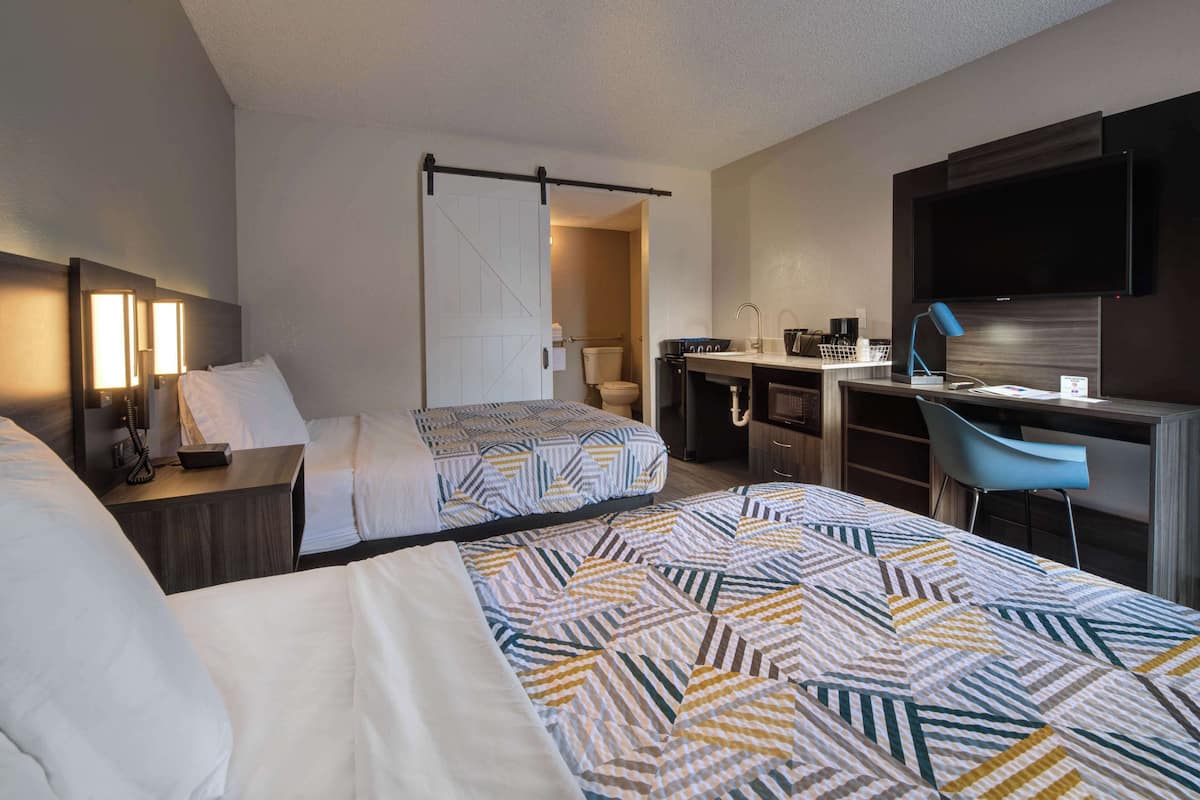 A hotel room with two beds, a desk with a chair, a TV, and a bathroom visible through an open door.