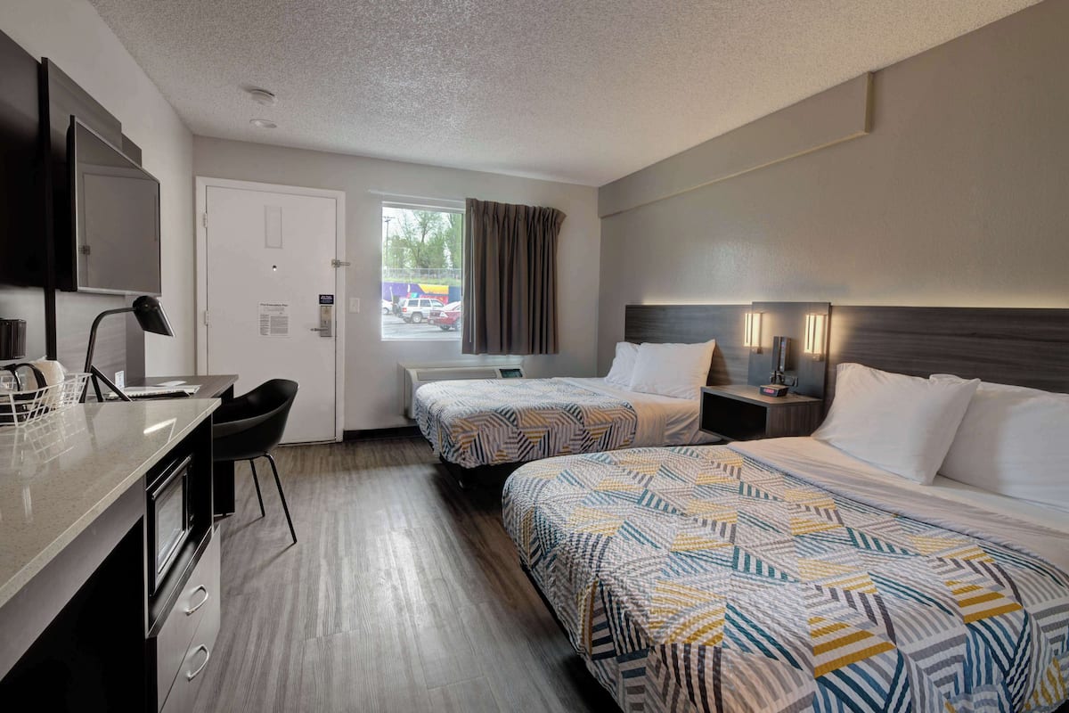 A hotel room with two beds, a desk, a chair, a TV, and a window with curtains.