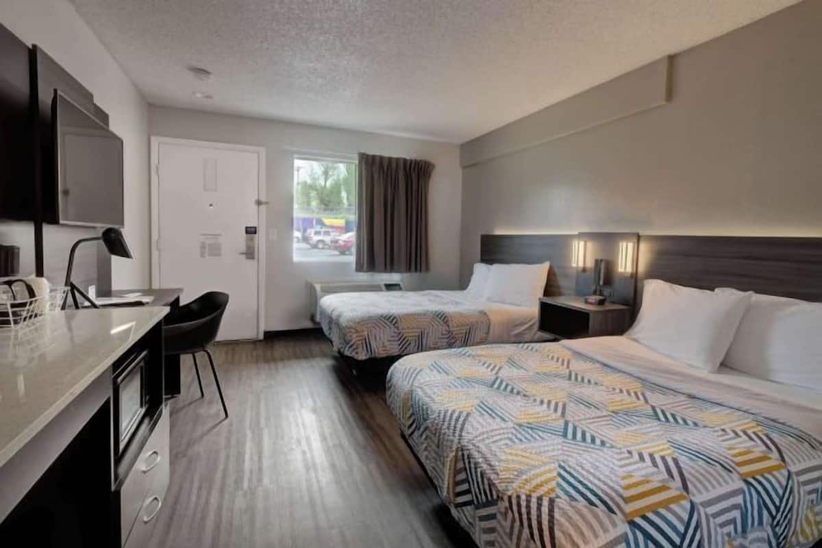 A hotel room with two beds, a desk, a chair, a TV, and a window with curtains.
