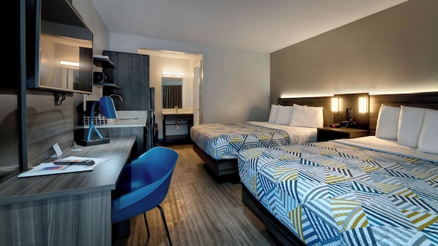 Ein Hotelzimmer mit zwei Betten, einem Schreibtisch, einem Stuhl, einem Fernseher und einem Badezimmer.