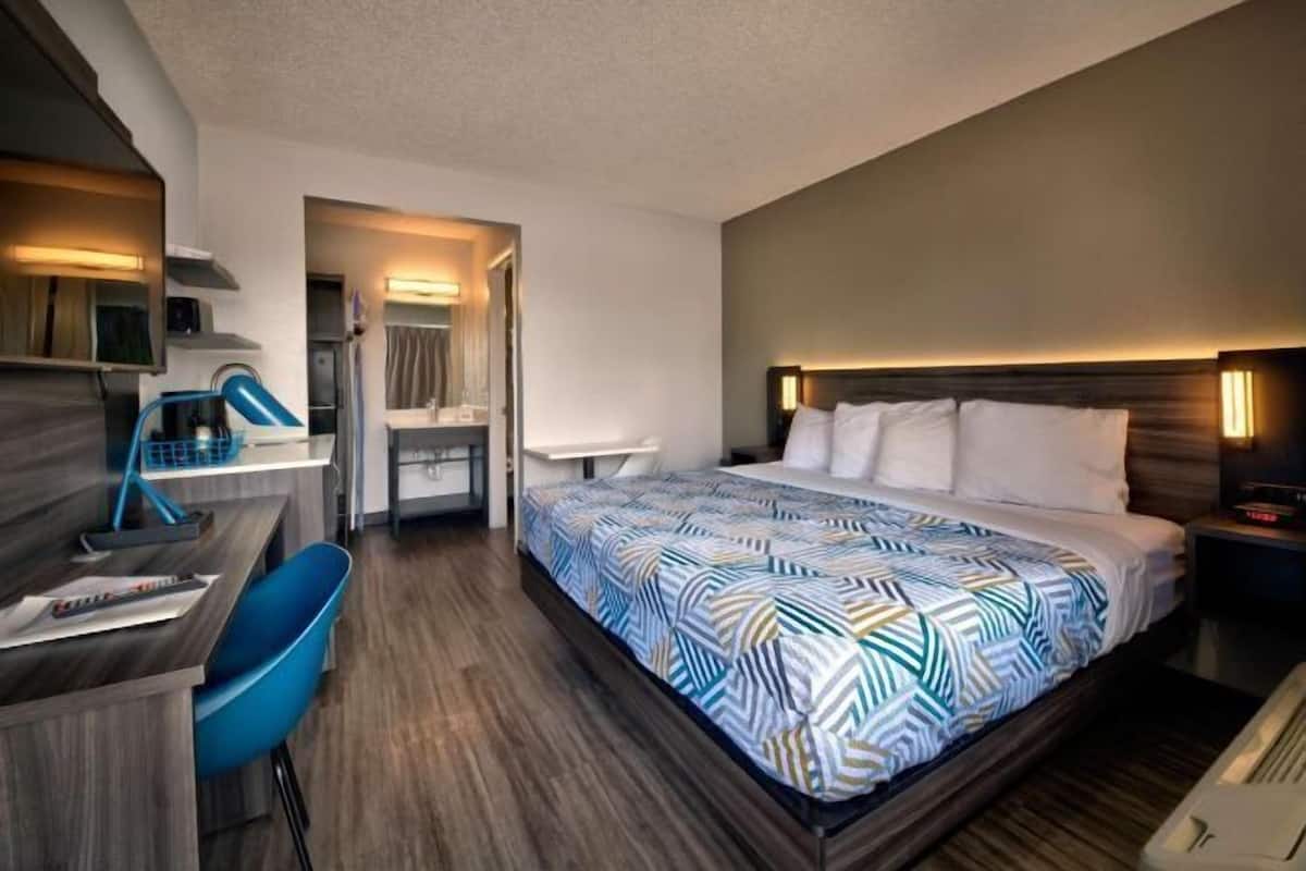 A hotel room with a bed, desk, chair, and a mirror.