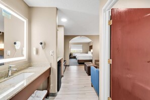 A hotel corridor with a bathroom on the left, a bed area in the center, and a red door on the right. - Comfort Suites Lakewood - Denver (Lakewood)