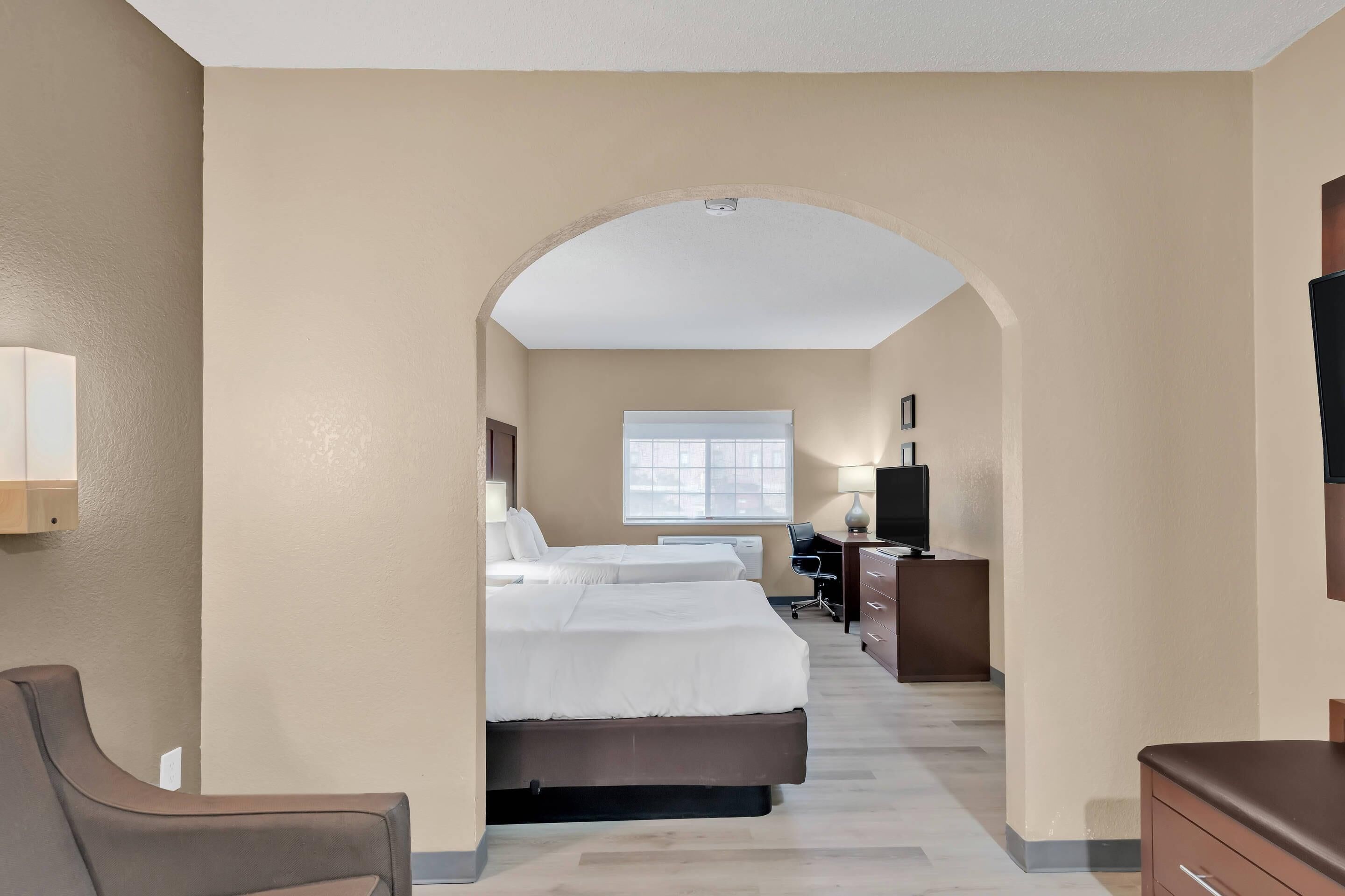 A hotel room with a bed, desk, chair, and TV.