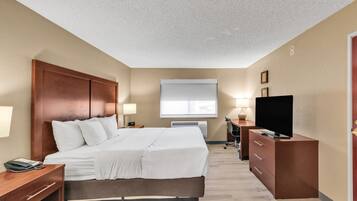 A hotel room with a large bed, a desk with a computer, a TV, and a window with blinds.