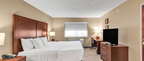 A hotel room with a large bed, a desk with a computer, a TV, and a window with blinds.