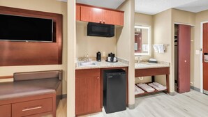 Habitación de hotel compacta con kitchenette, televisor de pantalla plana, microondas, lavamanos y un refrigerador pequeño.
